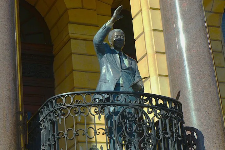 Eine Bronzestatue von Nelson Mandela, der von einem Balkon winkt.